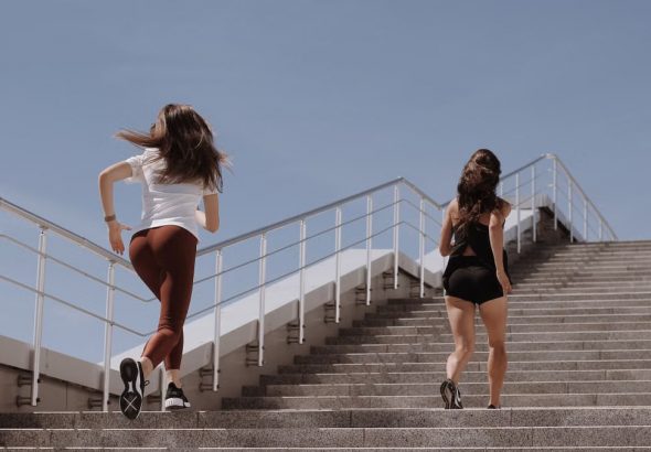 Two women running up outdoor stairs for fitness under a clear blue sky.